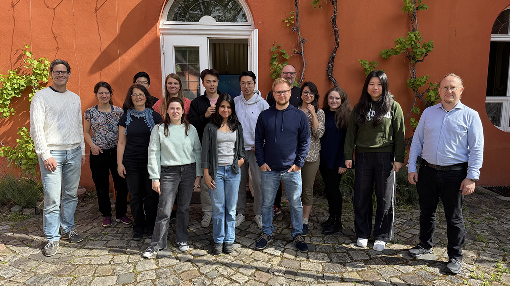 Group photo of a diverse team of researchers standing in front of an orange building.